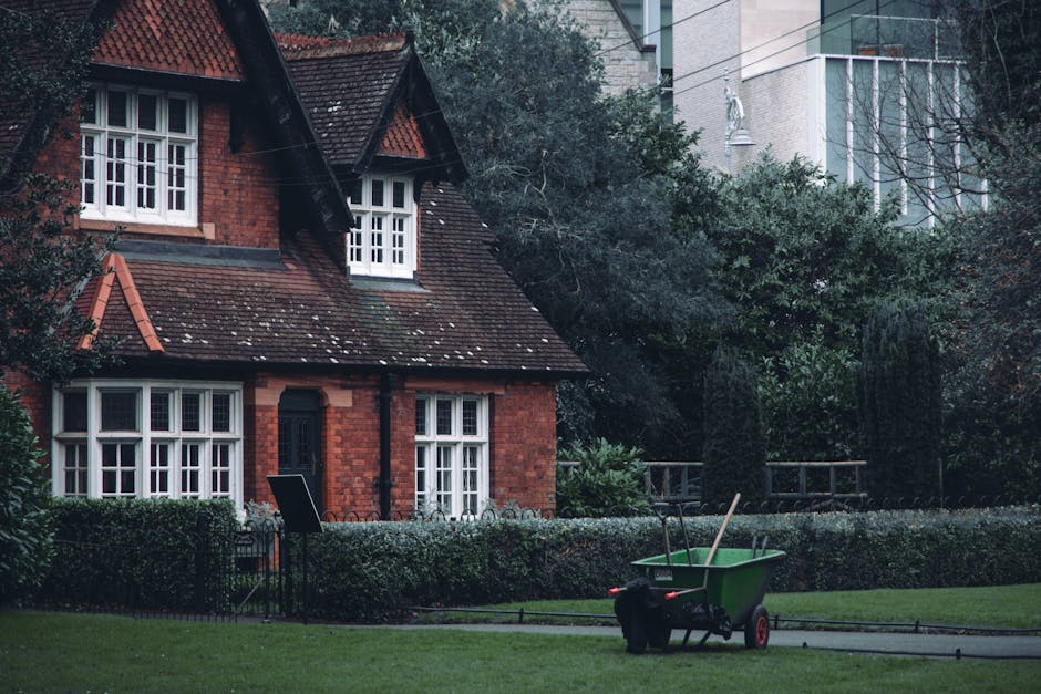 A cozy garden seating area featuring rustic wooden furniture painted in a soft green hue, including a bench with a slatted backrest and a matching armchair. The scene is lush with greenery, comprising